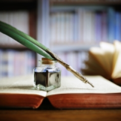 Quill pen and ink well resting on an old book in a library concept for literature, writing, author and history
